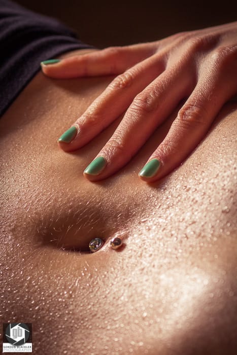 wet skin close up of woman's hand, stomach and belly button piercing