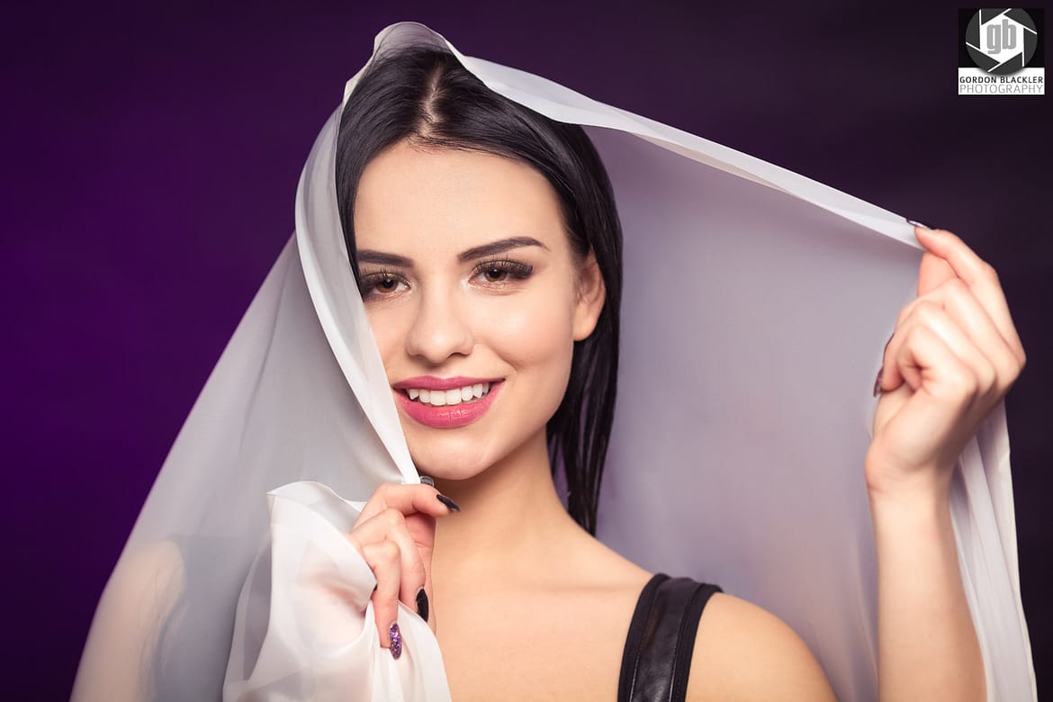 studio portrait of beautiful brunette who holds a white veil over her head