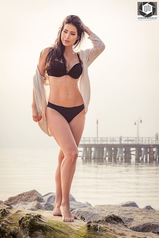 fashion portrait of beautiful brunette who stands on the rocks on the beach in sopot, poland