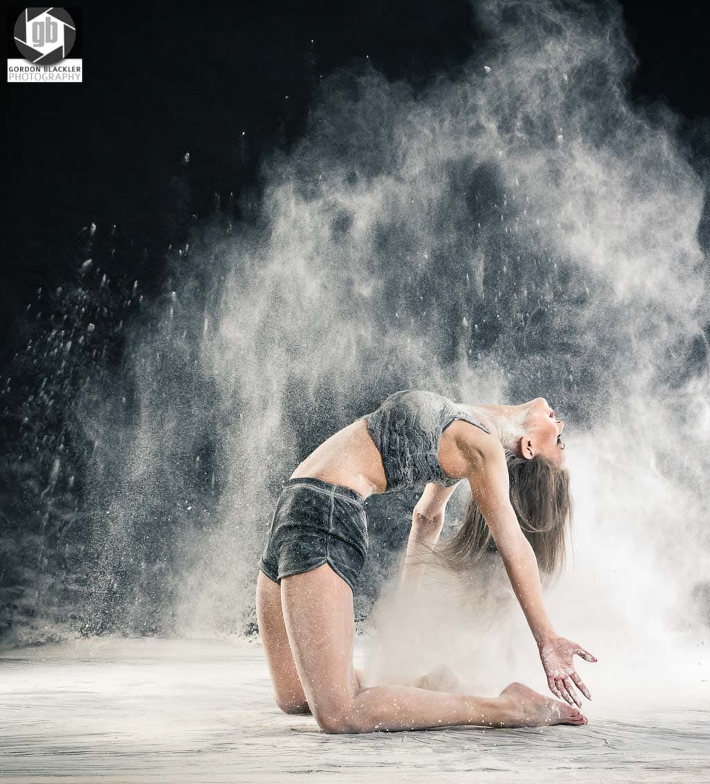 studio portrait of beautiful brunette dancer on her knees who throws powder in the air